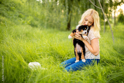 A beautiful girl with a dog sits in the park on the grass. Love to the animals. Home pet on a walk. Animal protection. Bernese mountain dog puppy.