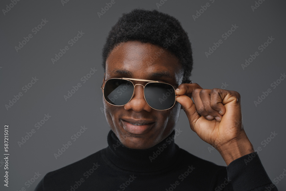 Fototapeta premium Shot of isolatedon grey background african man holding his sunglasses.