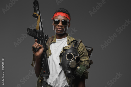 Studio shot of military man of african ethnic with red headband and rifle.