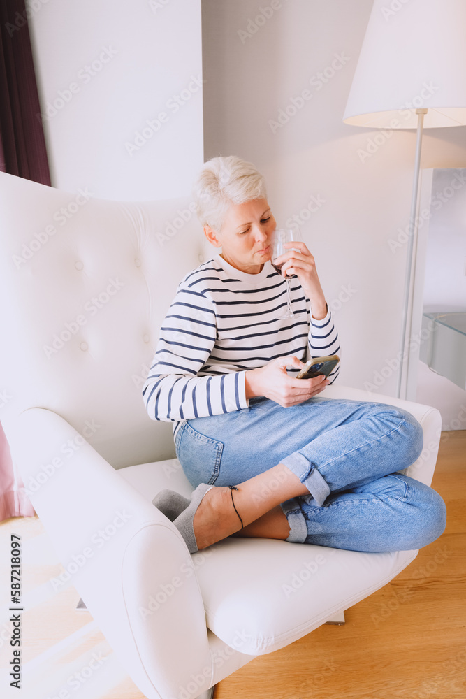 Sad blonde woman drinking red wine and checking bad news in her mobile phone Sad blonde woman drinking red wine and checking bad news in her mobile phone