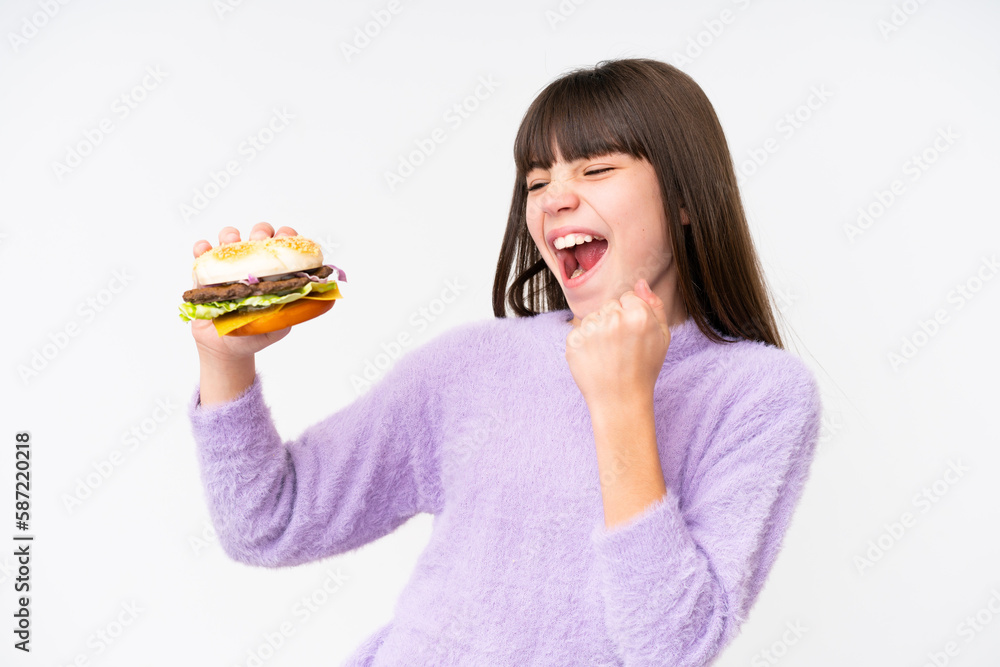 Little caucasian girl holding a burger over isolated background celebrating a victory Little caucasian girl holding a burger over isolated background celebrating a victory