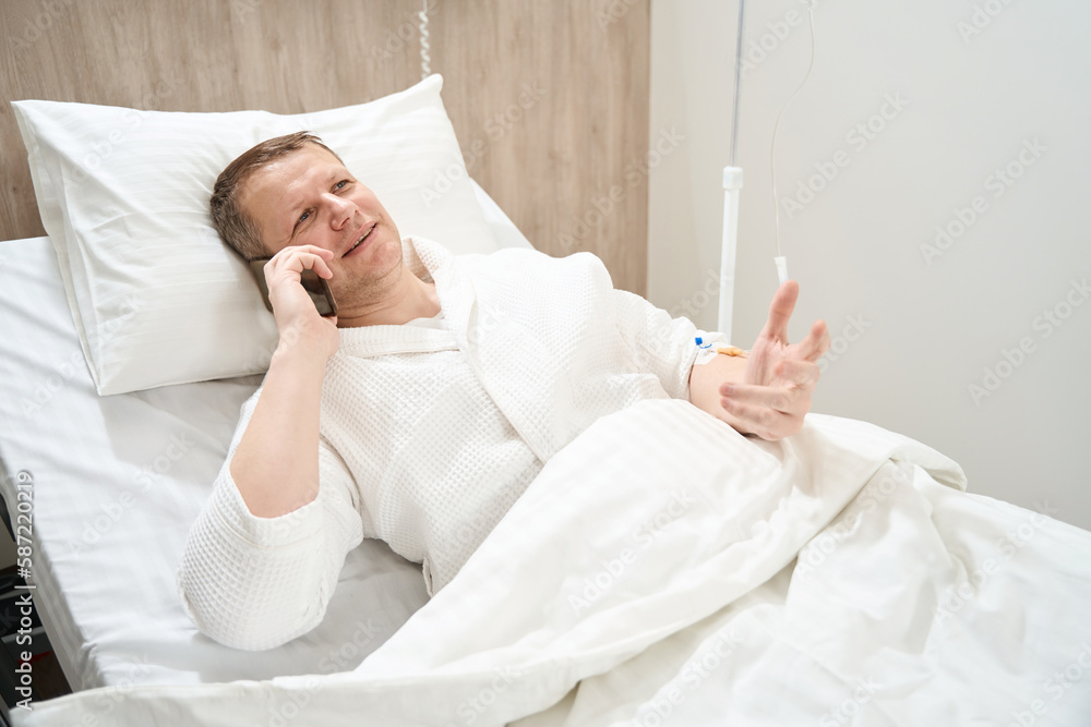 Man getting professional treatment in the modern clinic while using smartphone Man getting professional treatment in the modern clinic while using smartphone