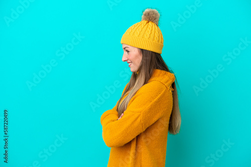 Young caucasian woman wearing winter jacket isolated on blue background in lateral position