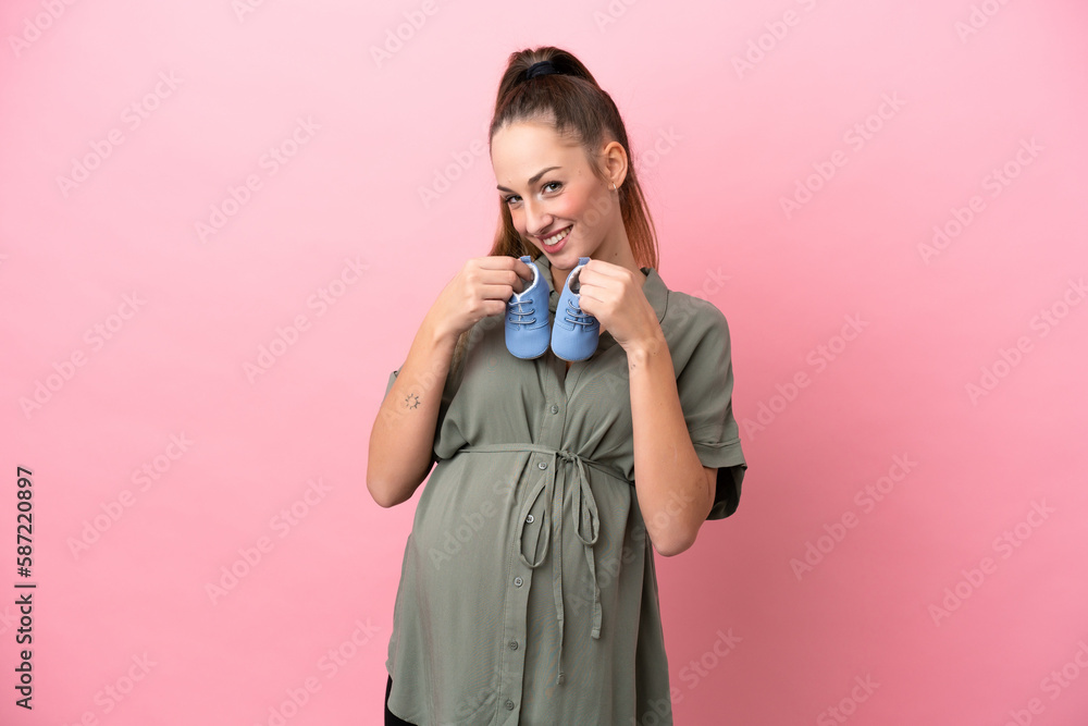 Young woman isolated on pink background pregnant and holding baby booties Young woman isolated on pink background pregnant and holding baby booties