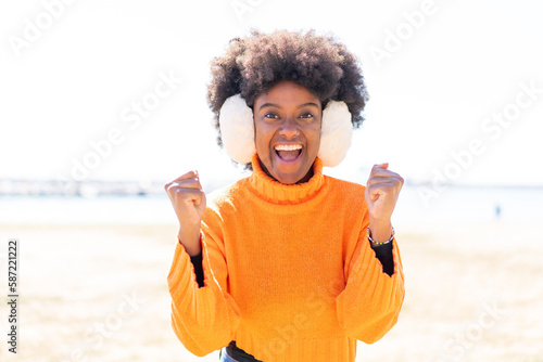 African American girl wearing winter muffs at outdoors celebrating a victory in winner position