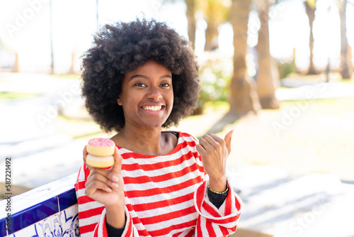African American girl holding a donut at outdoors pointing to the side to present a product