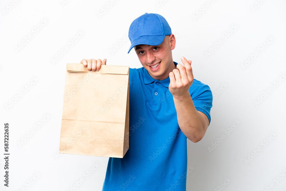 Young Brazilian man taking a bag of takeaway food isolated on white background making money gesture Young Brazilian man taking a bag of takeaway food isolated on white background making money gesture