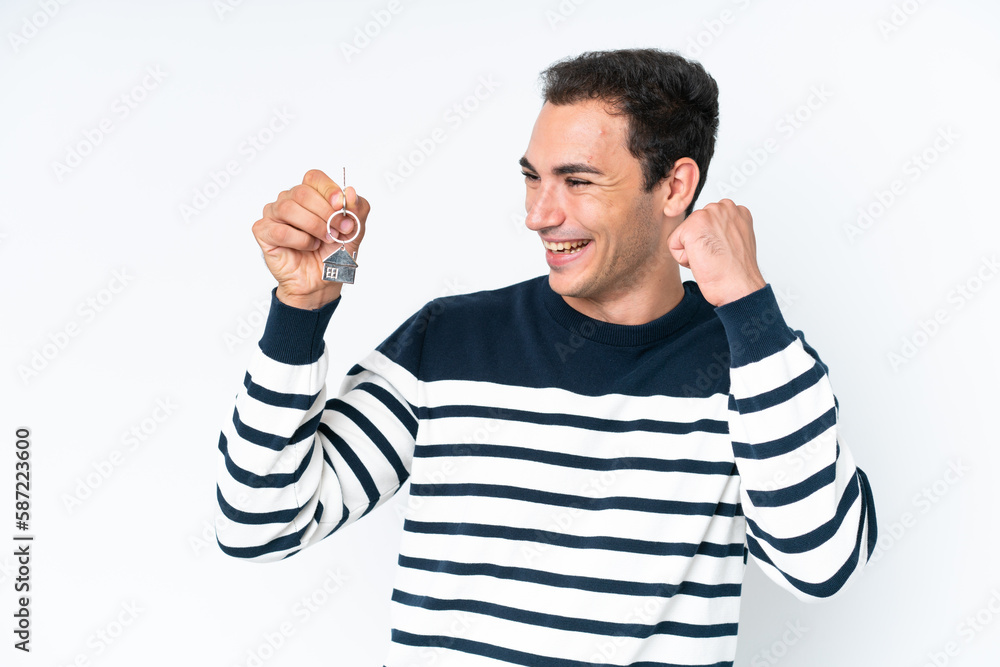 Fototapeta premium Young caucasian man holding home keys isolated on white background celebrating a victory