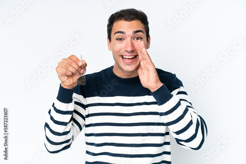 Young caucasian man holding home keys isolated on white background shouting with mouth wide open