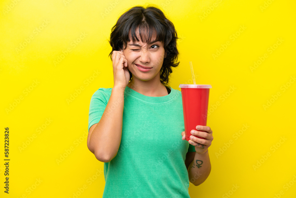Young Argentinian woman holding a soda isolated on yellow background frustrated and covering ears Young Argentinian woman holding a soda isolated on yellow background frustrated and covering ears