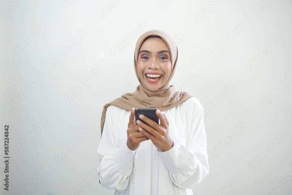 Beautiful smiling Asian Muslim woman wearing hijab Using mobile phone, typing sms message isolated on white background studio portrait. People religious lifestyle concept Beautiful smiling Asian Muslim woman wearing hijab Using mobile phone, typing sms message isolated on white background studio portrait. People religious lifestyle concept