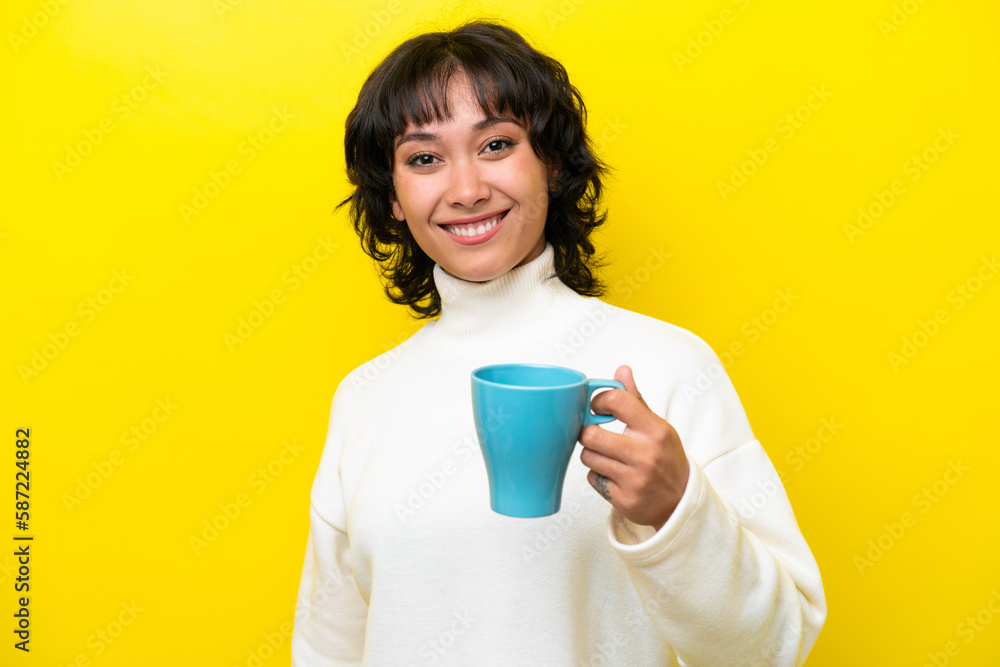 Young Argentinian woman holding cup of coffee isolated on yellow background with happy expression Young Argentinian woman holding cup of coffee isolated on yellow background with happy expression