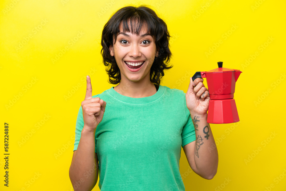 Young Argentinian woman holding coffee pot isolated on yellow background pointing up a great idea