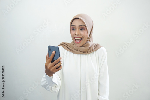Excited beautiful Asian muslim woman showing mobile phone isolated over white background