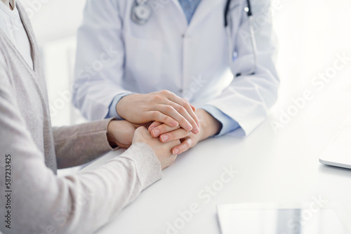 Doctor and patient sitting at the table in clinic office. The focus is on female physician s hands reassuring woman  only hands close up. Medicine concept