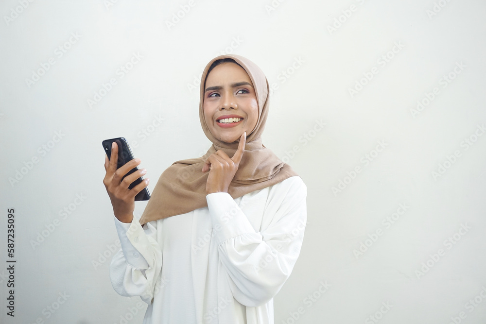 Excited beautiful Asian muslim woman showing mobile phone isolated over white background Excited beautiful Asian muslim woman showing mobile phone isolated over white background