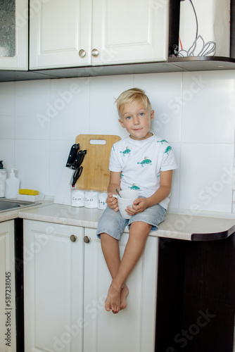 Happy relaxed young boy sitting in the kitchen, smiling, laughing, enjoying