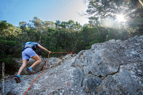 foto panoramica di una costa della Sardegna mentre un escursionista compie una" ferrata" nella parete rocciosa