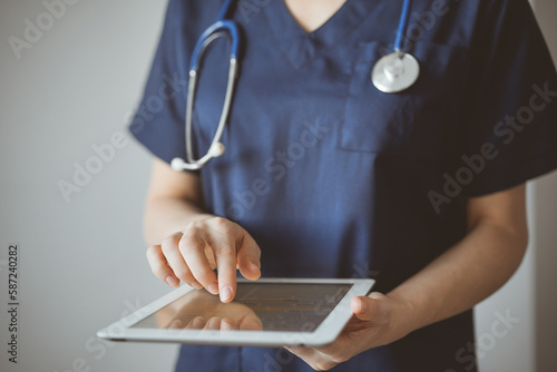 Doctor woman using tablet computer while standing near panorama window in clinic, close up. Physician or surgeon at work. Medicine concept photo