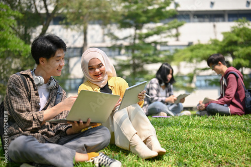 Two Asian college students are working on their schoolwork while sitting on the grass