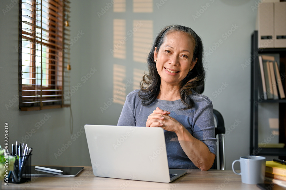 Successful Asian-aged businesswoman sits at her desk in her modern office. Successful Asian-aged businesswoman sits at her desk in her modern office.
