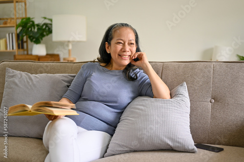 Smiling and happy Asian-aged retired woman relaxing on a sofa in her living room.