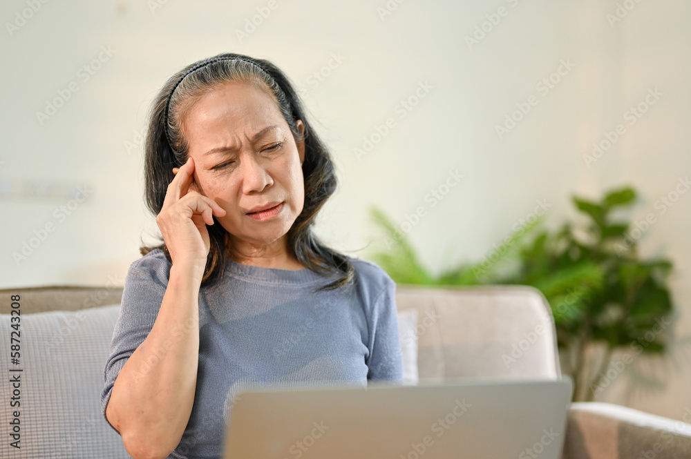Unwell senior Asian woman suffering from her headache or migraine Unwell senior Asian woman suffering from her headache or migraine