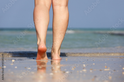 Barefoot girl walking by sea waves. Female legs on a wet sand, beach vacation and workout