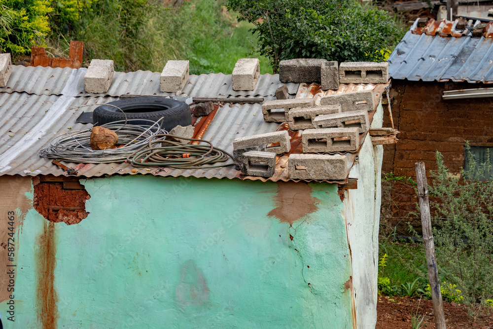 Bricks are stacked on the corrugated iron roof of a roughly built rural hut. Bricks are stacked on the corrugated iron roof of a roughly built rural hut.