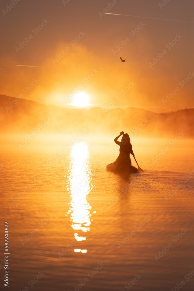 Vertical shot of a female silhouette sailing on a lake at bright golden hour
