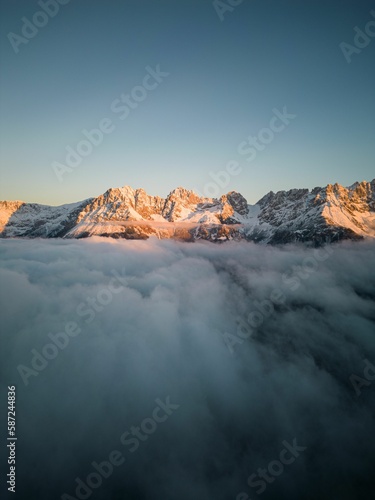 Vertical shot of a snowy mountain range covered with clouds at golden hour