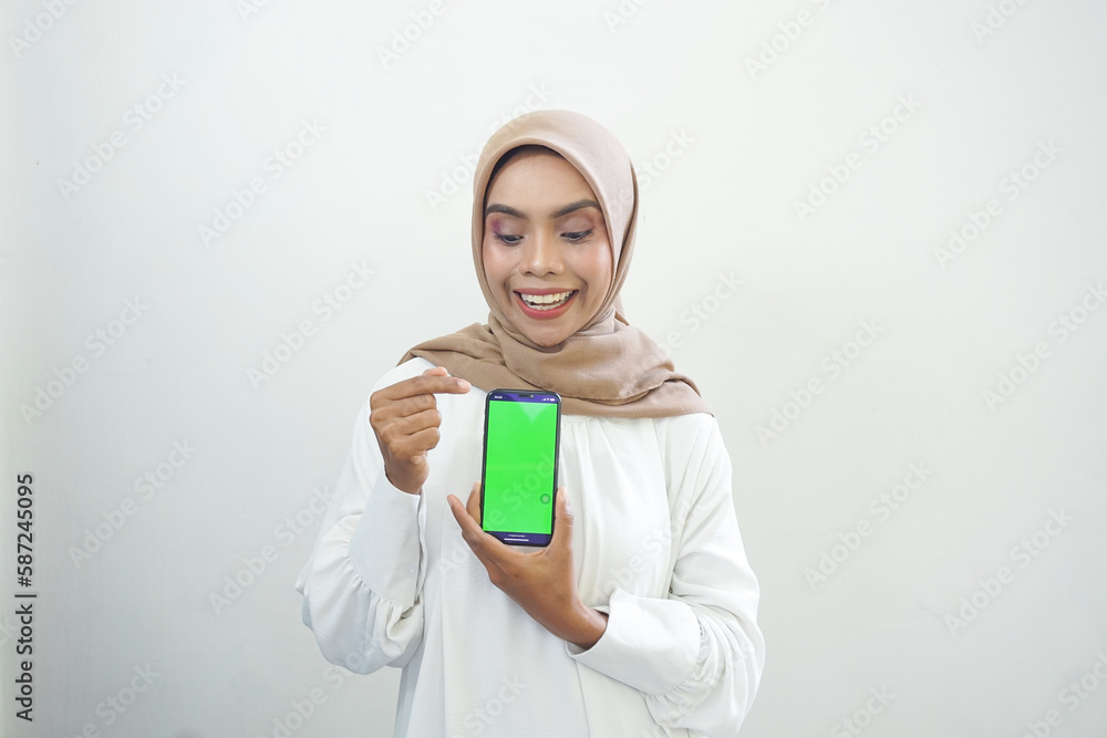 Excited beautiful Asian muslim woman showing green screen mobile phone isolated over white background. Excited beautiful Asian muslim woman showing green screen mobile phone isolated over white background.