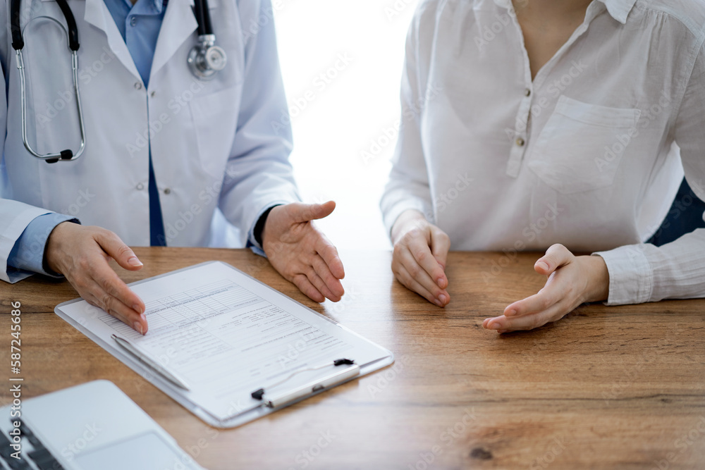 Doctor and patient discussing something while sitting near each other at the wooden desk in clinic, view from above. Medicine concept Doctor and patient discussing something while sitting near each other at the wooden desk in clinic, view from above. Medicine concept