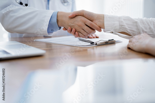 Fototapeta Naklejka Na Ścianę i Meble -  Doctor and patient shaking hands above the wooden table in clinic. Medicine concept