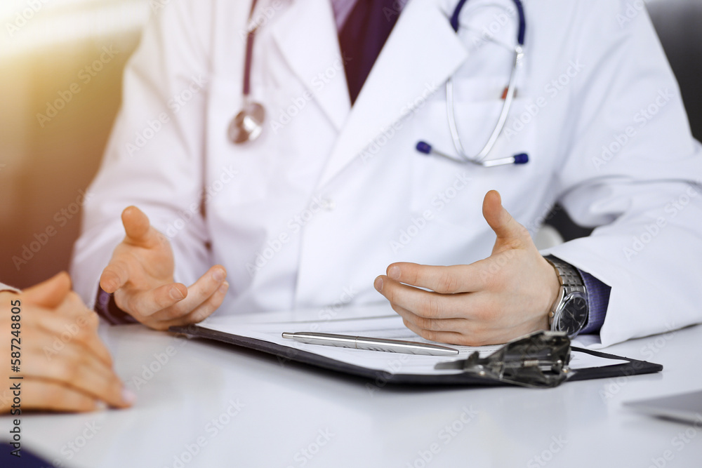 Unknown male doctor and patient woman discussing something while sittingin a darkened clinic, glare of light on the background. Close-up of hands Unknown male doctor and patient woman discussing something while sittingin a darkened clinic, glare of light on the background. Close-up of hands
