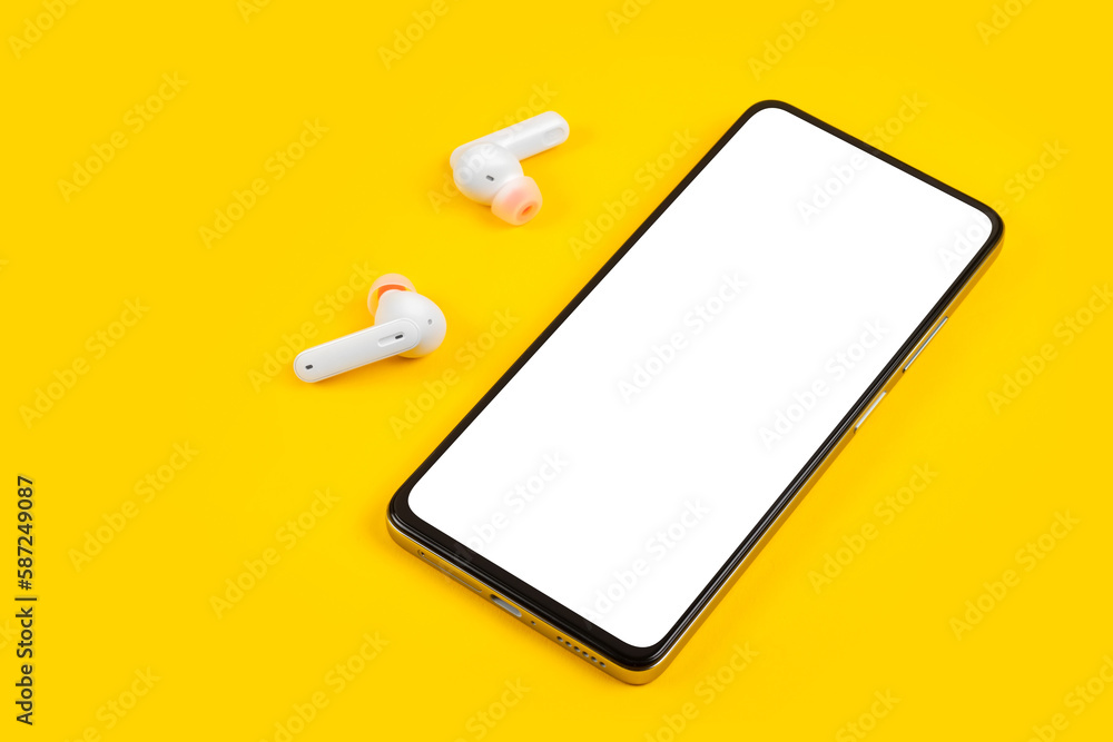 Mobile phone with empty screen and earphones on yellow surface. Wireless earphones, mobile phone on yellow background Mobile phone with empty screen and earphones on yellow surface. Wireless earphones, mobile phone on yellow background