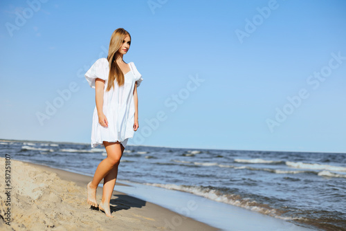 Fototapeta Naklejka Na Ścianę i Meble -  Happy smiling beautiful woman is walking on the ocean beach in a white summer dress