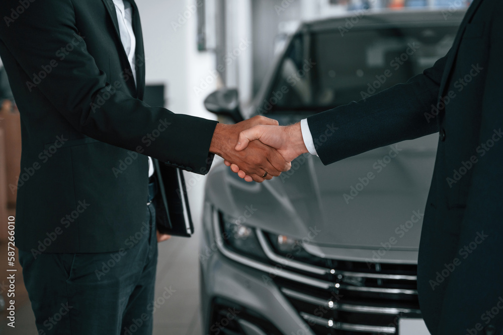 Close up view. Two businessmen are standing in the car showroom and making a deal, handshake Close up view. Two businessmen are standing in the car showroom and making a deal, handshake