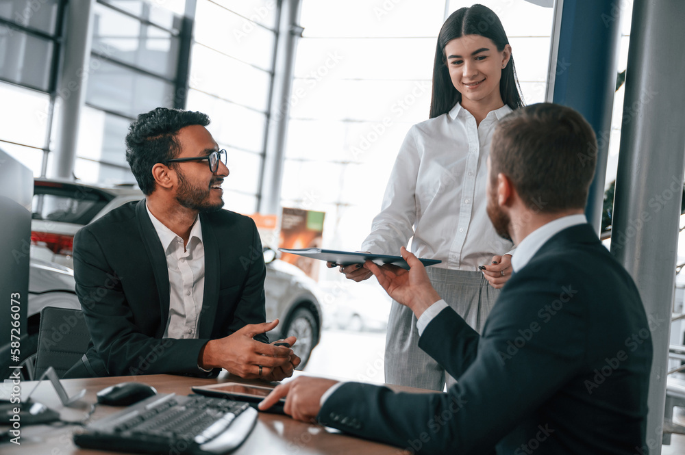 Woman is giving documents. Three people are working together in the car showroom Woman is giving documents. Three people are working together in the car showroom