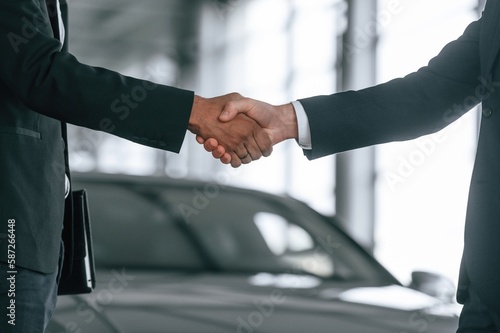 Close up view. Two businessmen are standing in the car showroom and making a deal, handshake © standret