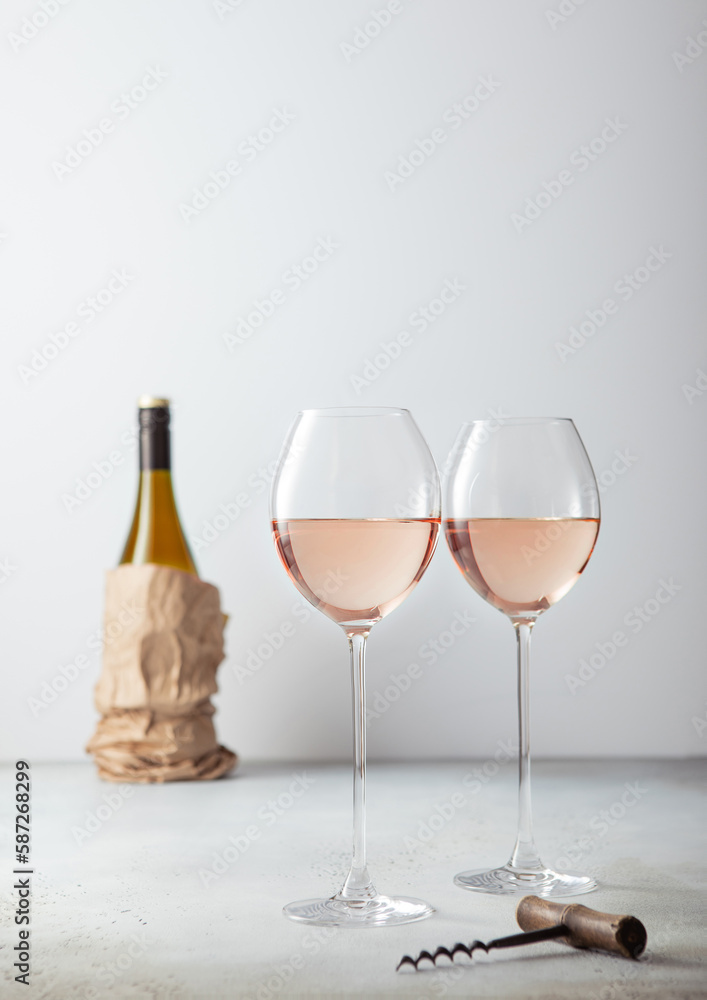 Pink rose glasses of wine with corkscrew and bottle on light background. Pink rose glasses of wine with corkscrew and bottle on light background.