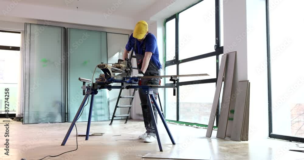 Worker cuts wooden boards for laying parquet with saw. Builder prepares floor covering material Worker cuts wooden boards for laying parquet with saw. Builder prepares floor covering material