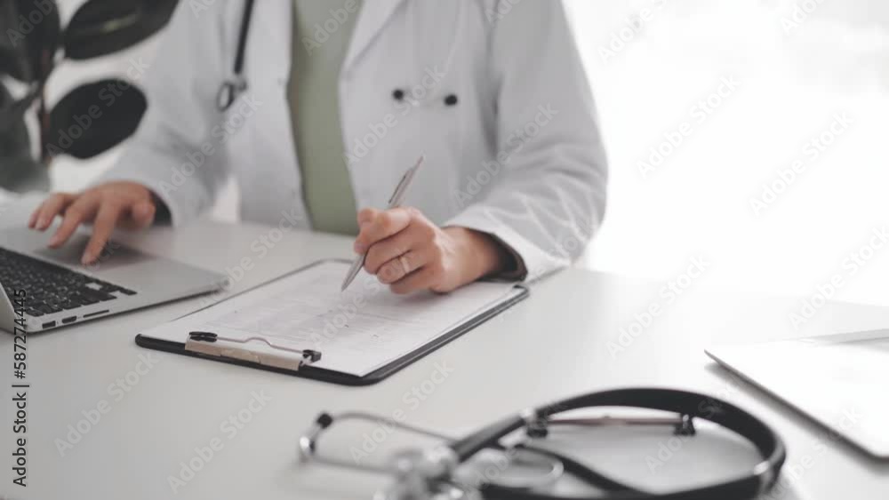 Unknown doctor woman sitting and writing notes at the white desk in clinic or hospital office, close up. Medicine concept Unknown doctor woman sitting and writing notes at the white desk in clinic or hospital office, close up. Medicine concept