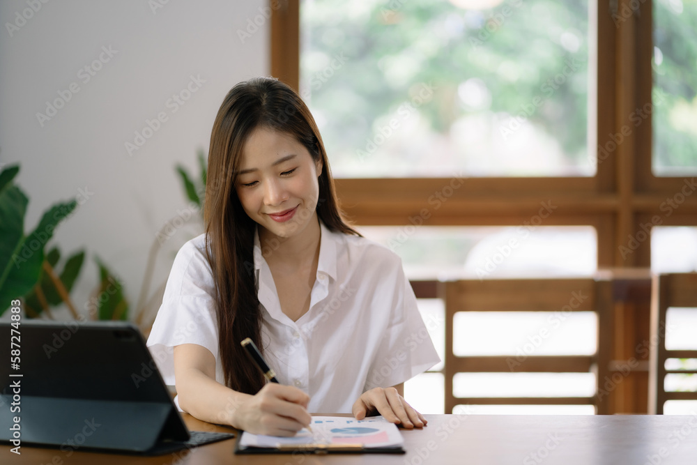 Cropped view of smiling beautiful woman writing in a journal while sitting at desk in office. Cropped view of smiling beautiful woman writing in a journal while sitting at desk in office.