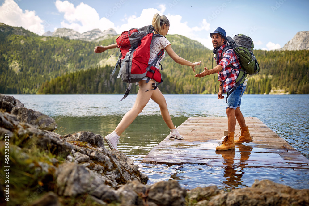 © luckybusiness - Young couple on wooden jetty by lake. Woman jumping, man lending a hand to her. Summer trip in nature. Lifestyle, togetherness, nature concept © luckybusiness - Young couple on wooden jetty by lake. Woman jumping, man lending a hand to her. Summer trip in nature. Lifestyle, togetherness, nature concept