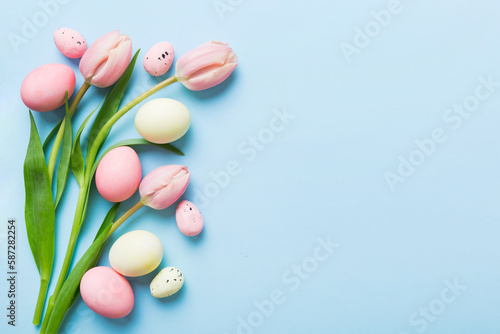 Happy Easter composition. Easter eggs on colored table with yellow Tulips. Natural dyed colorful eggs background top view with copy space