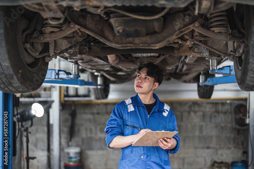 Vehicle service maintenance asian man checking under car condition in garage. Automotive mechanic maintenance checklist document. Car repair service concept