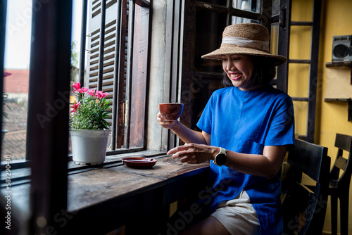 Female tourist in hat backpacking, Hoi An, Vietnam, sitting and drinking coffee for breakfast in a cafe. © Supavadee
