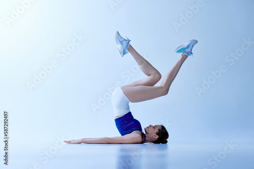 Flexible, athletic, sporty, young girl in sportswear training against light blue studio background. Strength and motivation. Concept of sport, healthy and active lifestyle, beauty, fitness