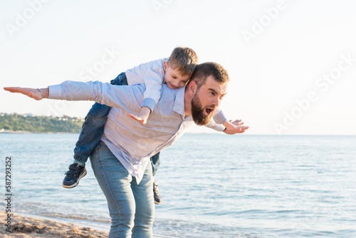 Father and son have fun on the summer beach. Father rolls his son on his back like a airplane. Concept: Travel and vacation, Fun time, family, father's day, sons, summer, vacation, summer mood